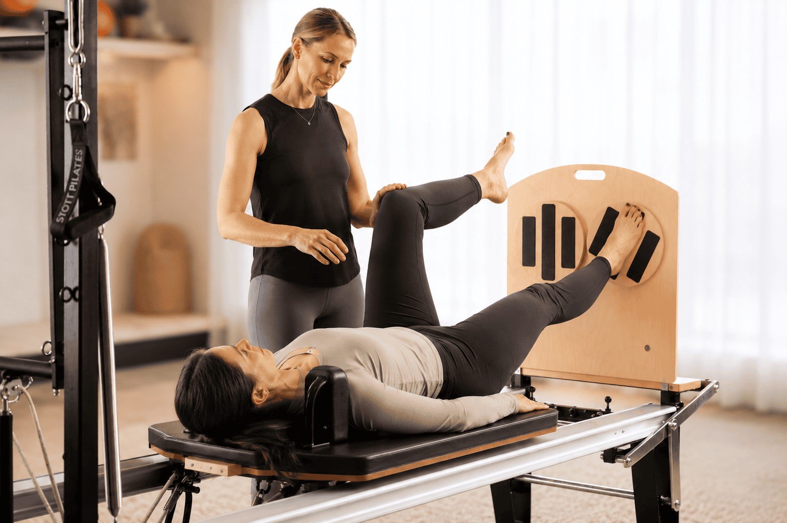 Pilates instructor guiding a client through a leg press exercise on the Reformer to build low back support and control