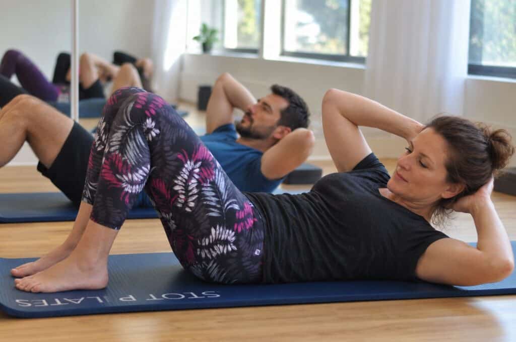 Two Pilates teacher training students performing a modified Obliques exercise with feet on the mat in a Portland studio
