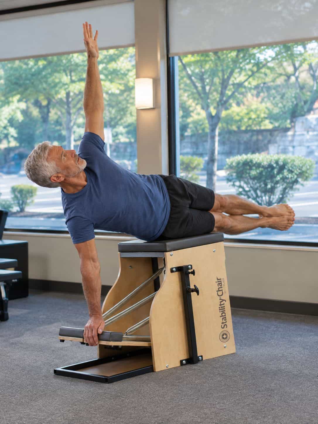 Man performing a side bend on a STOTT PILATES chair at Pacific Northwest Pilates in Portland, showing strength and control